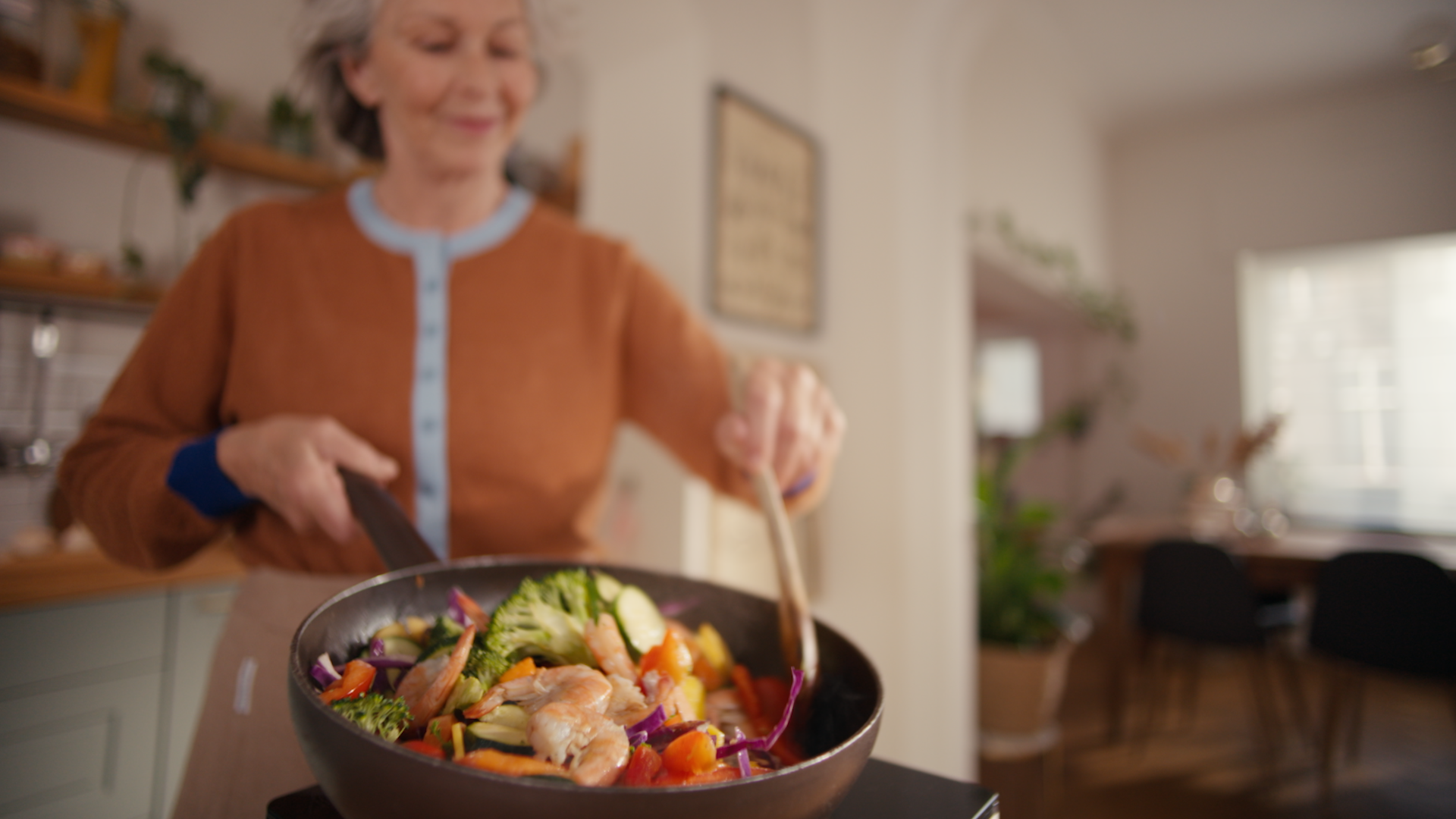 Usměvavá žena míchá krevety na pánvi přičemž vytváří kuchyňské pachy