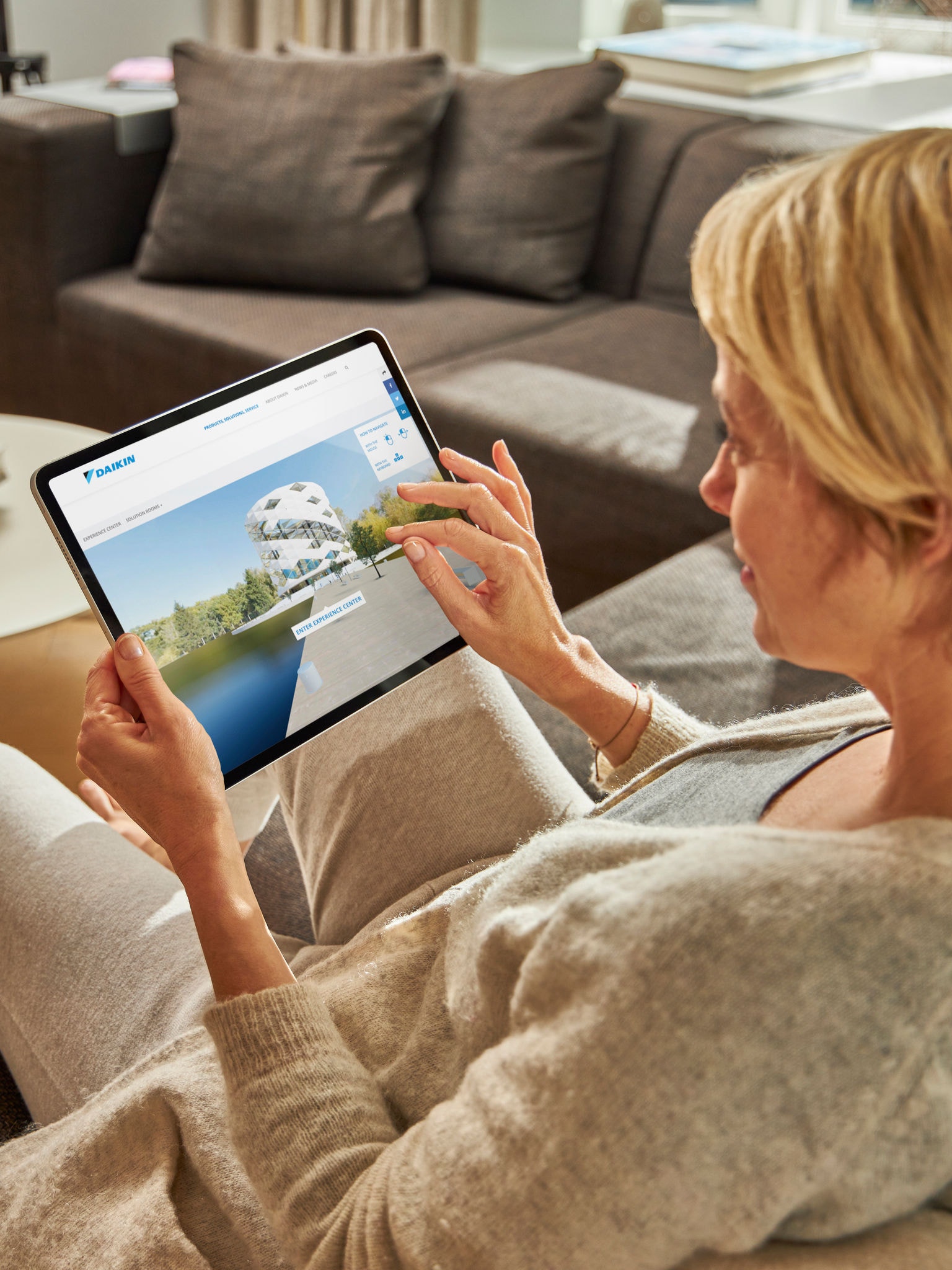 Žena sedící na pohovce a prohlížející si klimatizace ve virtuálním zážitkovém centru na svém tabletu