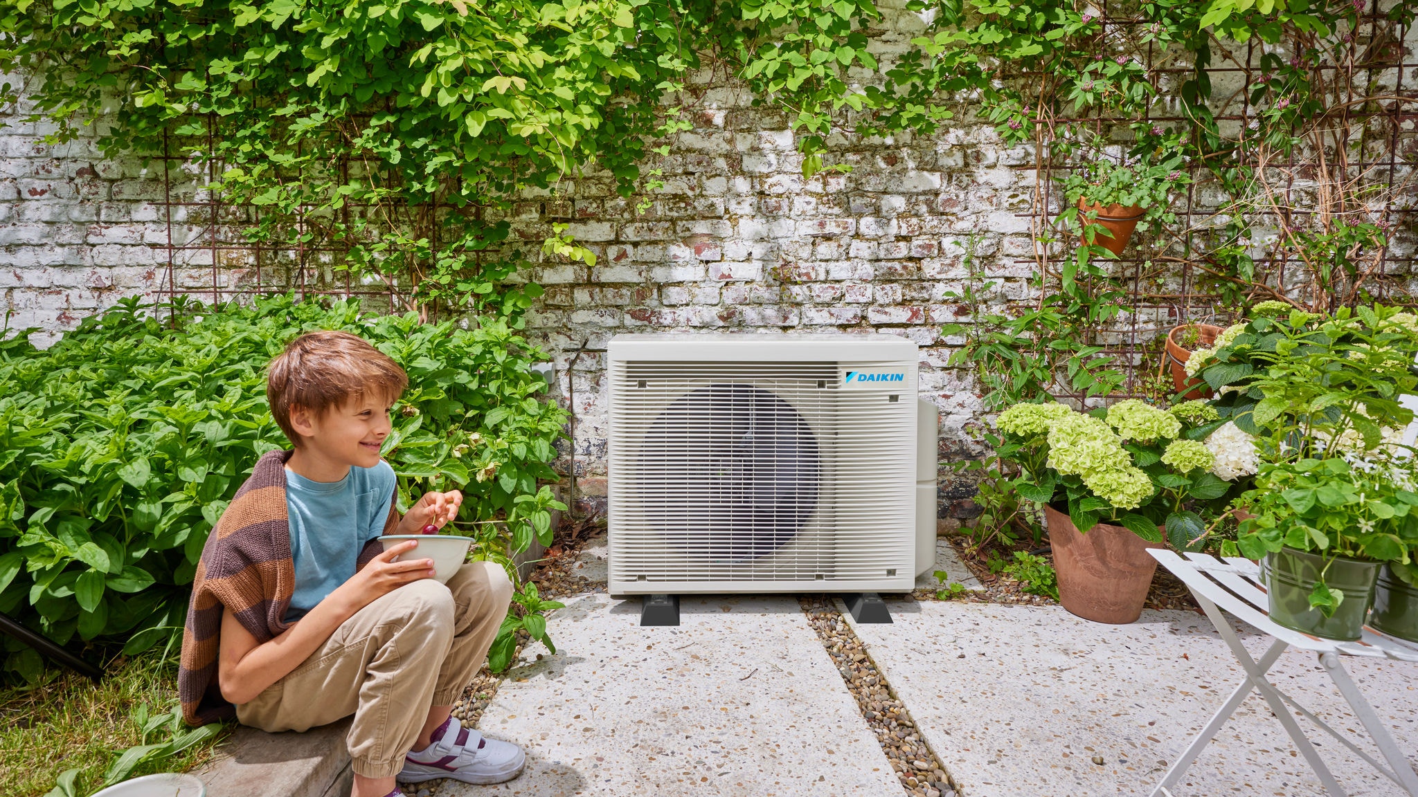 Dítě v blízkosti venkovní jednotky hybridního tepelného čerpadla Daikin, která spojuje energetickou účinnost s pěkným prostředím zahrady.