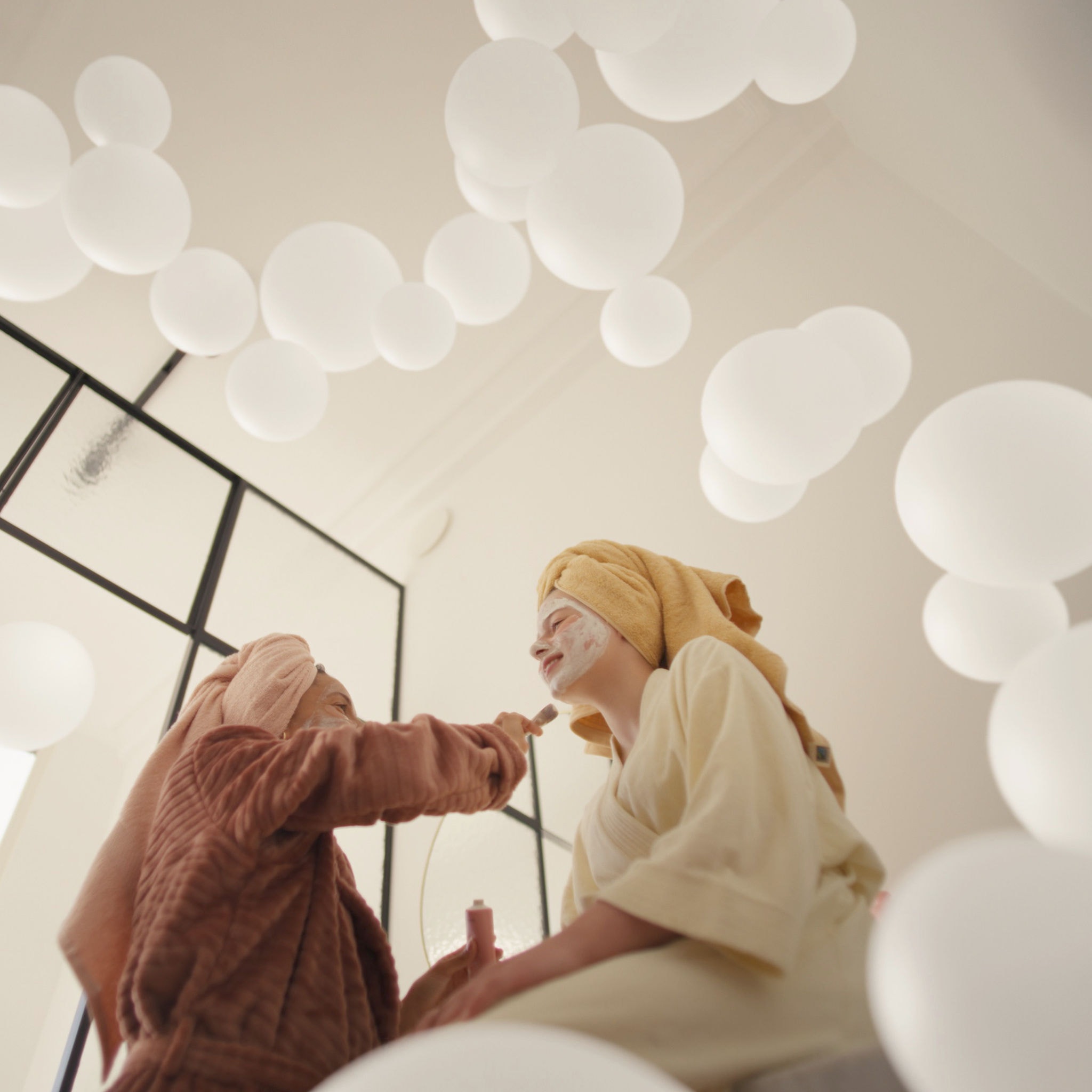 Matka a dcera si užívají péči o pleť s obličejovými maskami v dobře větrané místnosti, díky systému větrání s čerstvým vzduchem.