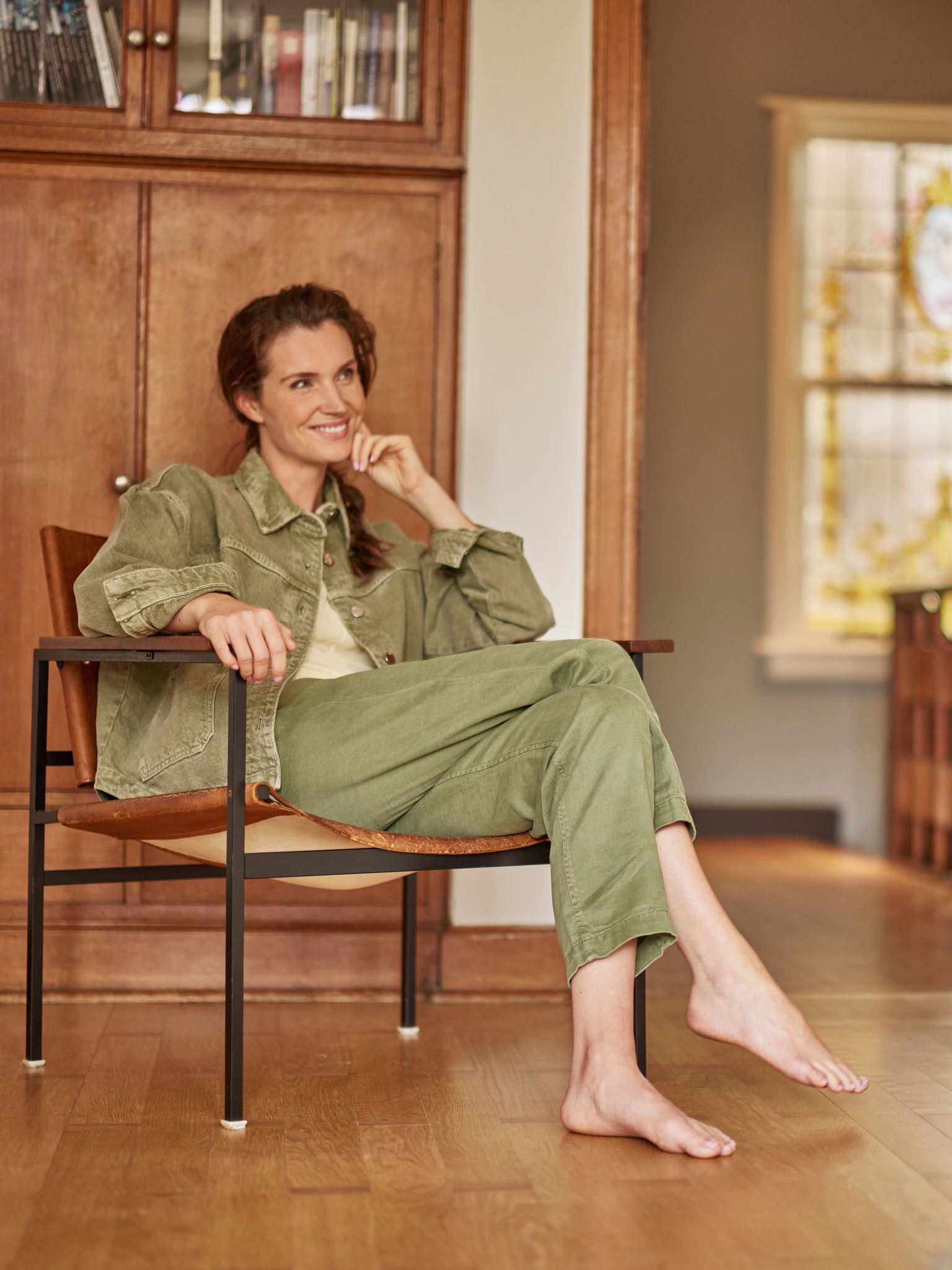 Žena sedí v křesle, bosá, usmívá se a dívá se před sebe