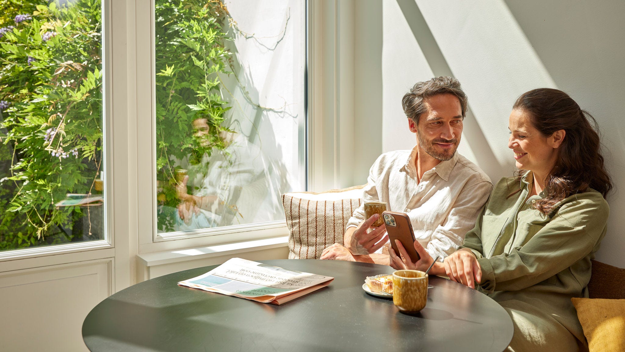 Pár si vychutnává kávu a kontroluje úspory energie na svém telefonu, který ukazuje snížení nákladů díky používání tepelného čerpadla.