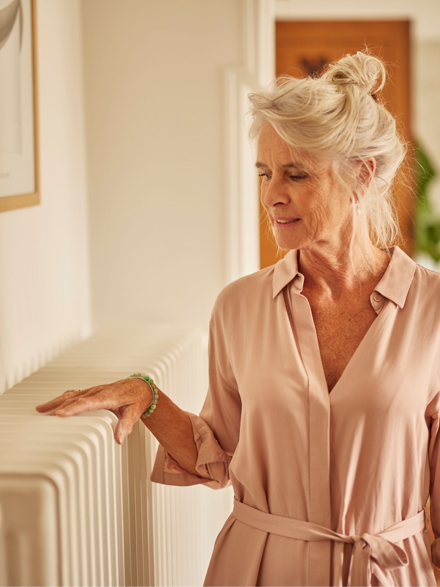 Žena si zahřívá ruce nad radiátorem spojeným s tepelným čerpadlem v ložnici