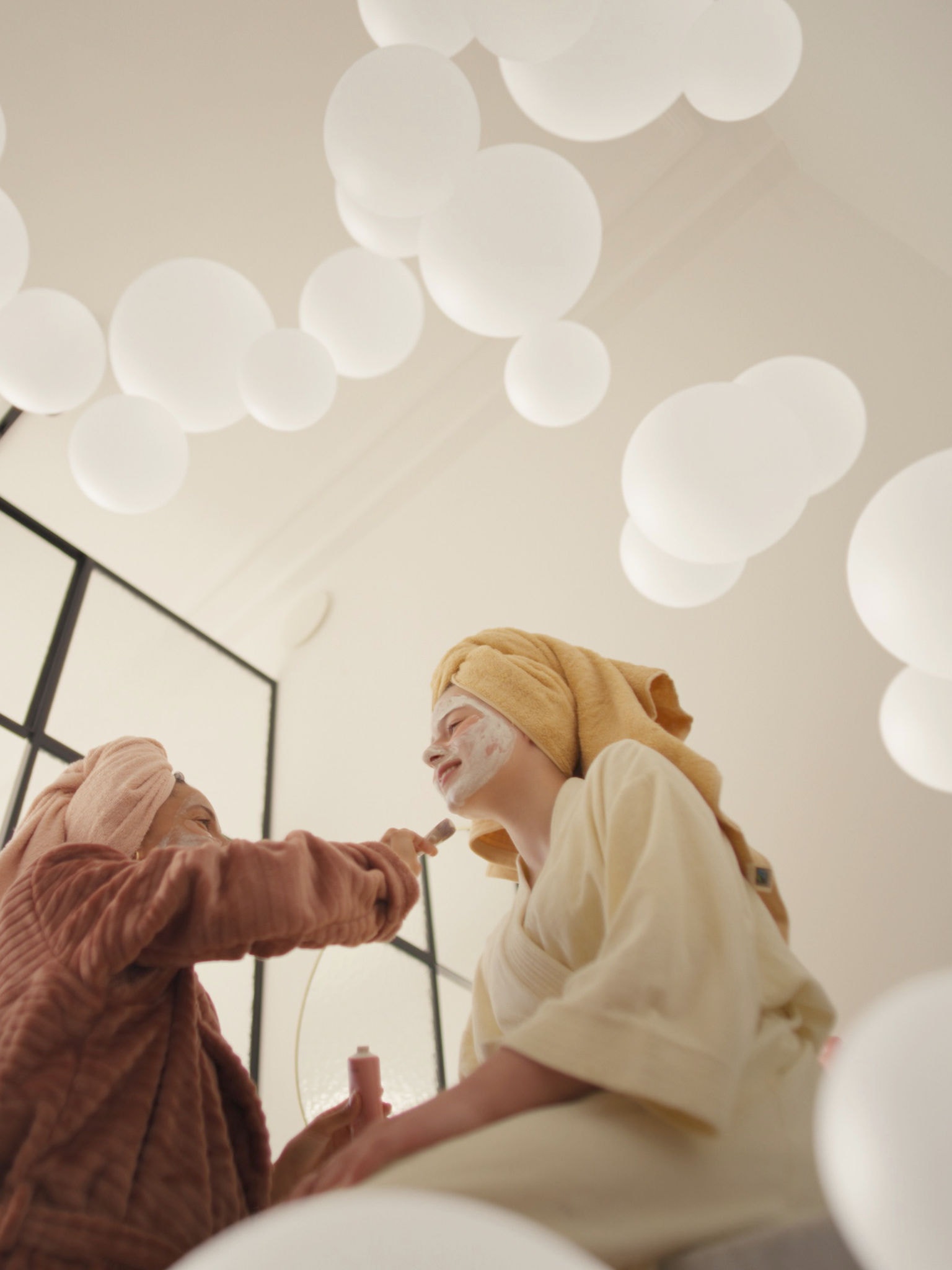 Matka a dcera si užívají péči o pleť s obličejovými maskami v dobře větrané místnosti, díky systému větrání s čerstvým vzduchem.