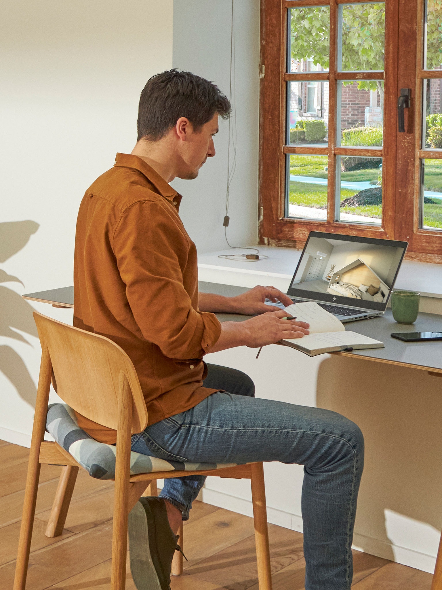 Muž stojící u okna a prohlížející si klimatizace ve virtuálním zážitkovém centru na svém notebooku