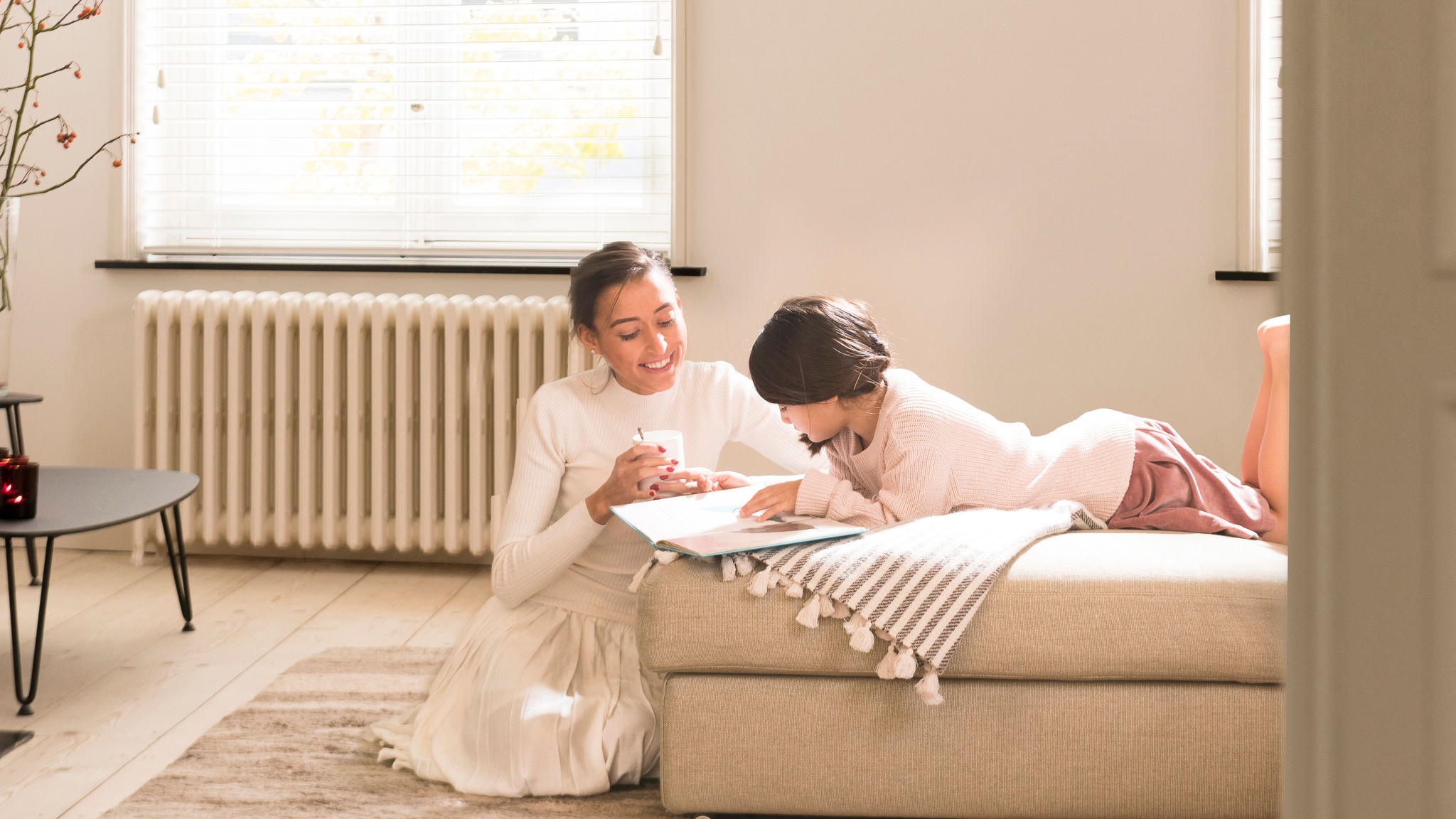 Matka pomáhá dceři číst knihu v útulném a teplém obývacím pokoji