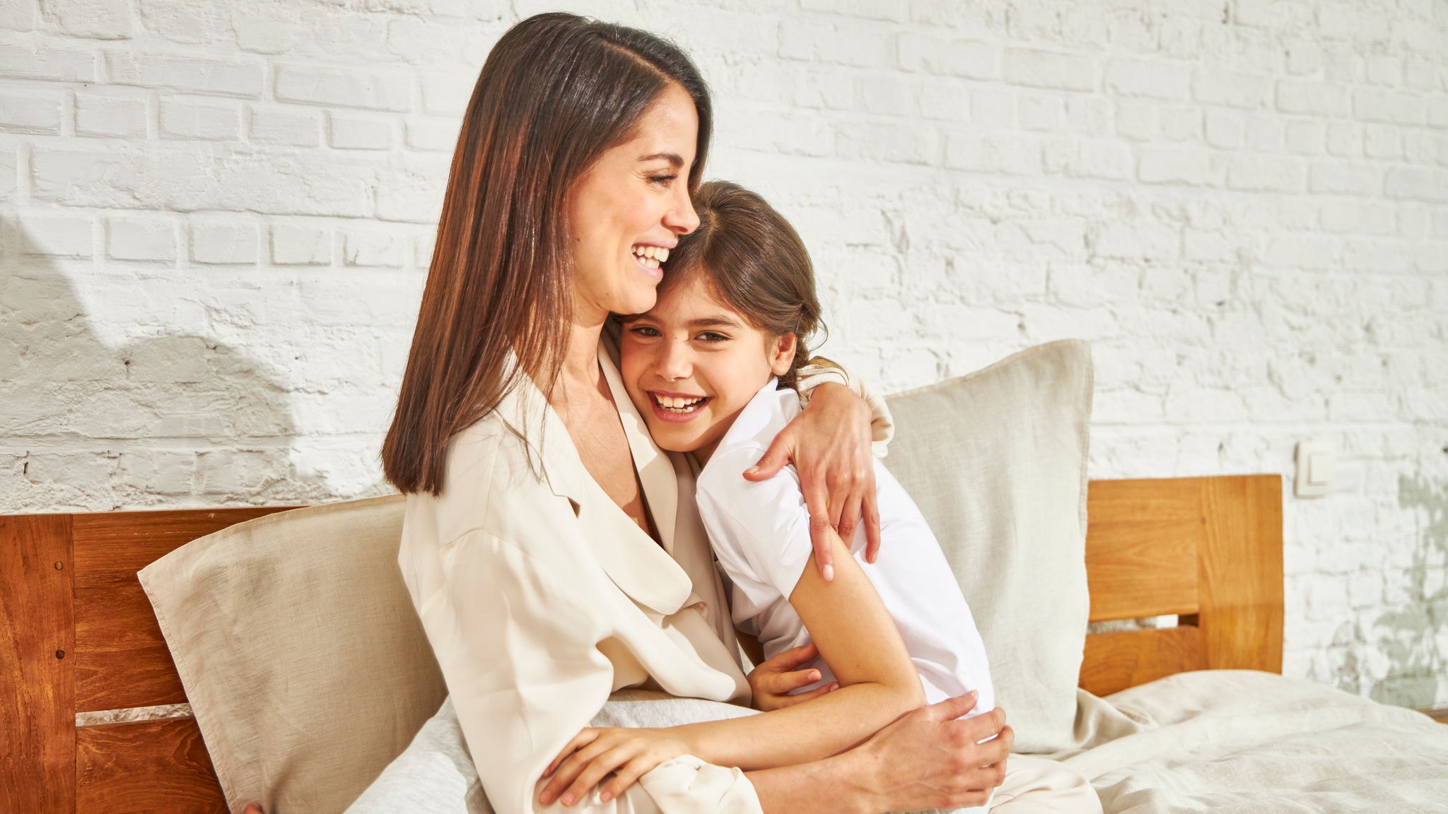 Matka a malá dcera se usmívají a objímají, zatímco sedí na posteli