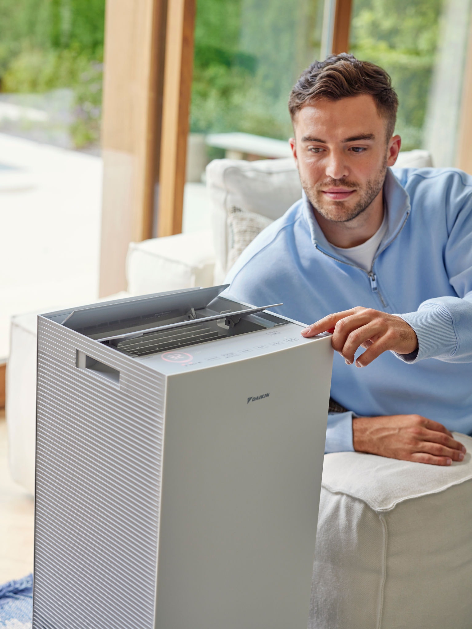 Muž nastavuje čističku vzduchu Daikin v obývacím pokoji, aby snížil množství alergenů z koček