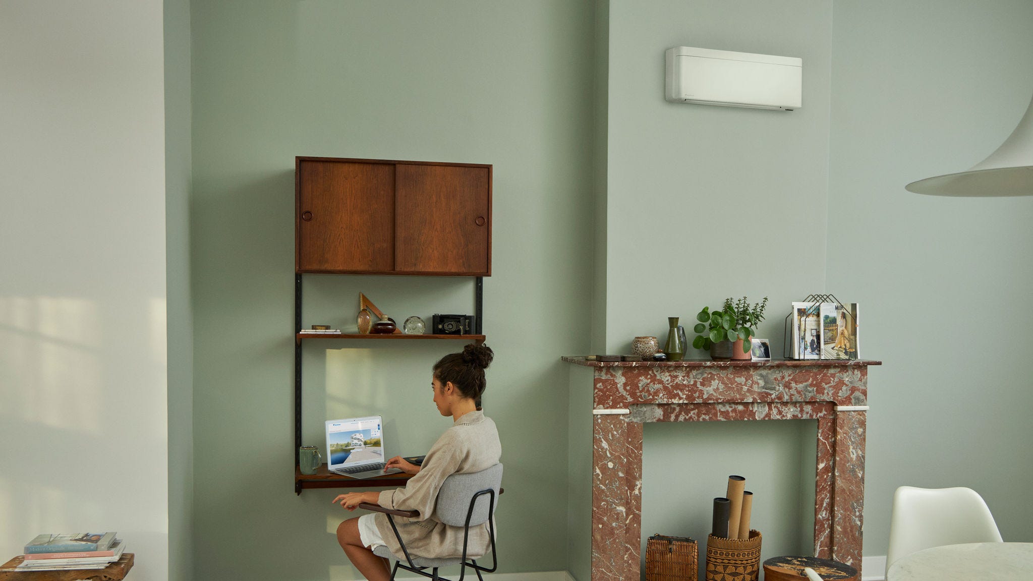 Žena navštěvující virtuální zážitkové centrum Daikin prostřednictvím notebooku u svého malého stolu v krásně zařízeném obývacím pokoji