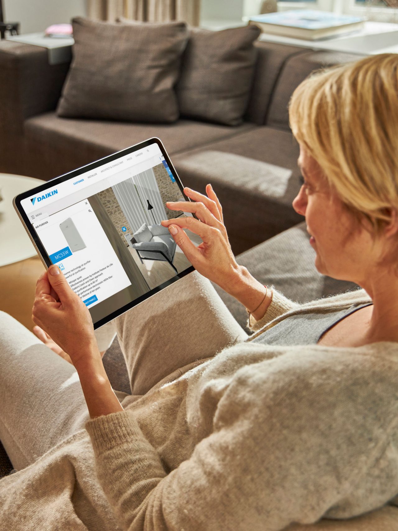 Žena sedící na pohovce a prohlížející si klimatizaci ve virtuálním zážitkovém centru na svém tabletu